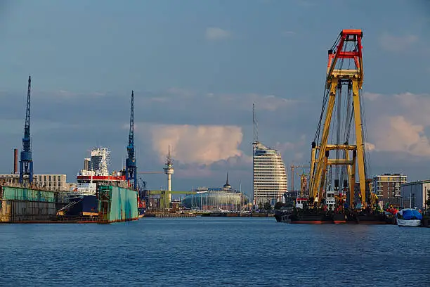 The inner city and skyline of Bremerhaven (Germany, federal state Bremen) taken from the harbour. In the foreground are some docks, ships, cranes and harbour installations.