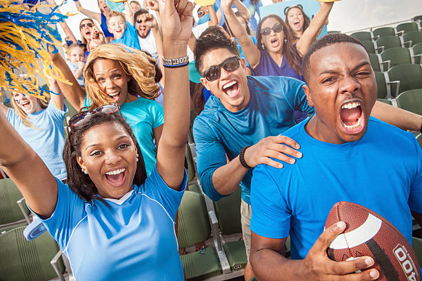 Football Crowd Cheering For Their Sports Team A large group of young adult football fans in outdoor stadium seats and dressed in blue clothing yell and cheer with excitement for their team. american football stadium stadium sport outdoors stock pictures, royalty-free photos & images