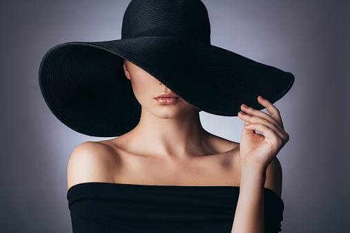 Portrait of an attractive and young blonde woman in a black hat and a leather trench coat while walking around the city. The concept of style and fashion.