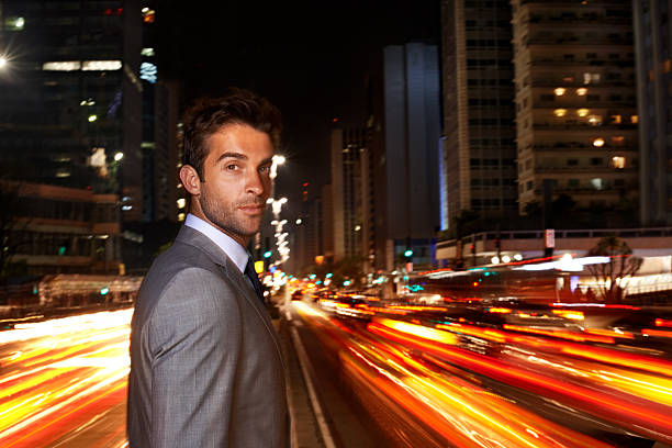 A portrait of a handsome businessman standing in the middle of a busy city street at night
