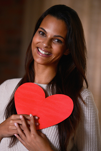 Portrait of an attractive ethnic female holding a heart shaped card indoors