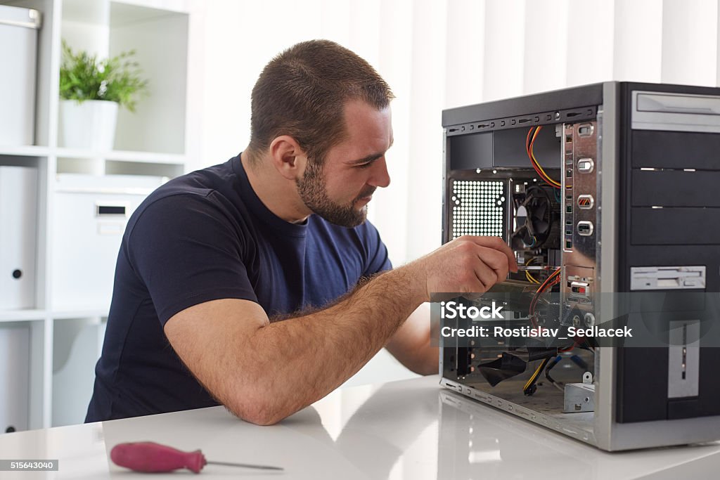 Man repairing computer Young man repairing computer while sitting at his working place Repairing Stock Photo
