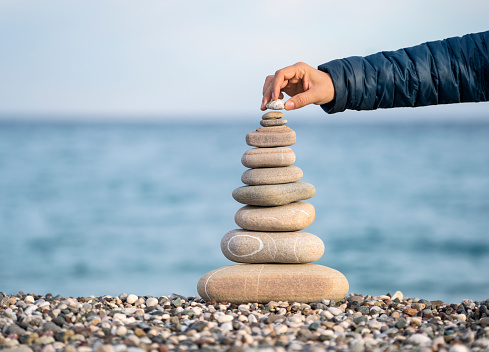 Man's hand balancing stack of stones on beach