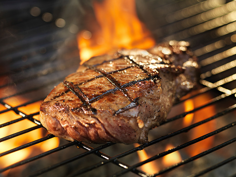 barbecueing steak on grill with flames
