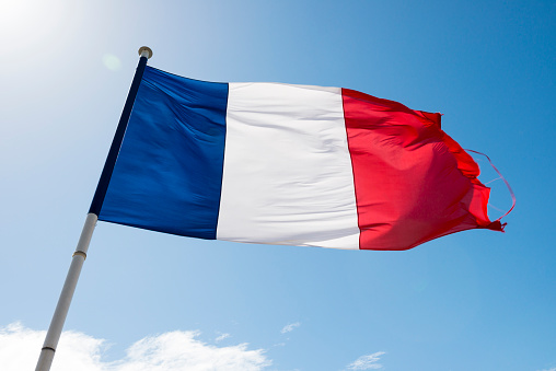 A slightly tattered French flag flies in a wind against a blue sky in France