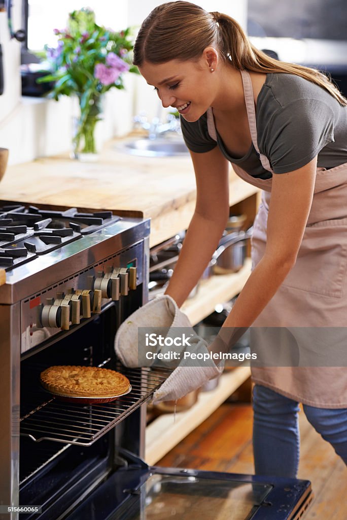 Baked to perfection Shot of an attractive young woman taking out a baked pie from the oven Oven Stock Photo
