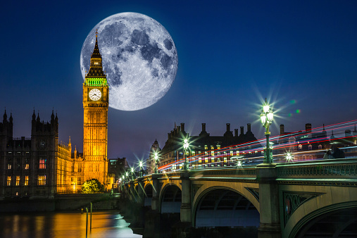 Twilight scene in London with Big Ben and the Houses of Parliament with a full moon and traffic on Westminster bridge