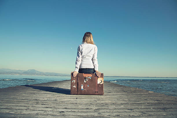 woman sitting on her suitcase waiting for the sunset stock photo