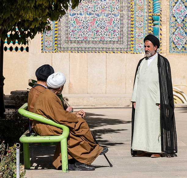 Mullahs, Khan Madrasa. Shiraz, Iran Shiraz, Iran - February 23, 2016: Two seated and one standing gown and turban clad mullahs converse in the courtyard of the Khan Madrasa, Shiraz, Iran. Canon EOS 5Ds, 165 mm. mullah photos stock pictures, royalty-free photos & images