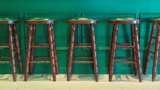 Row of wooden stools in front of green counter inside a vintage style bar.