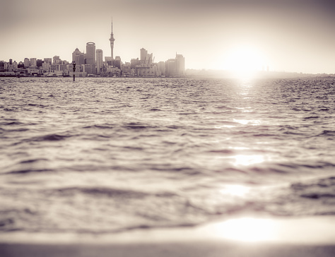Toned monochrome view of Auckland's Sky Tower and CBD silhouetted against a setting sun.