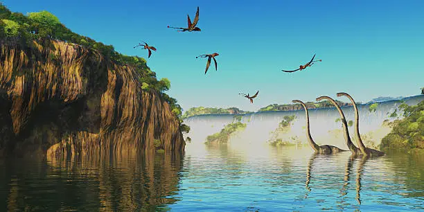 Omeisaurus herbivorous sauropod dinosaurs wade through a river below a waterfall as Dimorphodon flying reptiles fly overhead.