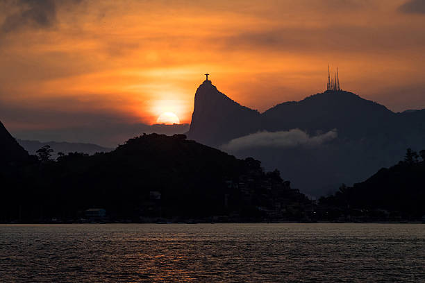 Sunset Behind Christ the Redeemer Statue, Rio de Janeiro, Brazil Sun setting behind the famous Christ the Redeemer statue atop the Corcovado Mountain in Rio de Janeiro, Brazil. cristo redentor rio de janeiro stock pictures, royalty-free photos & images