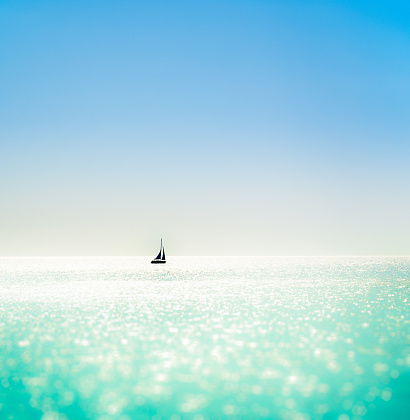 A distant small yacht just below the horizon, with a sparkling, colourful sea, and a clear blue sky.