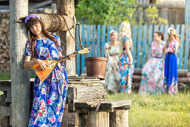 Beautiful country girl playing the balalaika at the well on a summer evening in a countryside