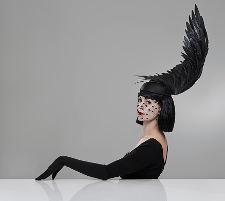 Shot of a young woman in a wing-shaped headpiece sitting in a studio
