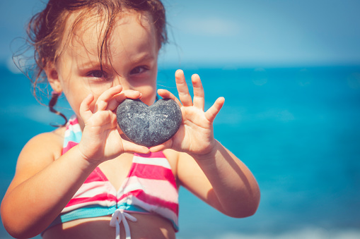 Happy little girl holding a stone in heart shape on the beach