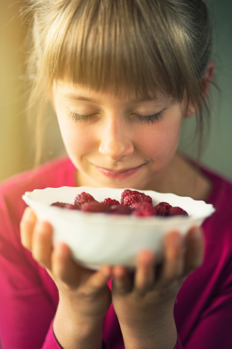 Smiling little girl smelling raspberries.