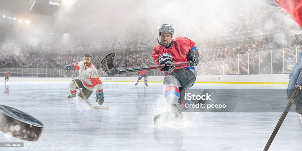 Ice Hockey Player Scoring Professional ice hockey player sliding on ice with one knee and having just hit puck during ice hockey game. Action takes place in a cold, misty indoor ice hockey arena full of spectators. All players are wearing generic icy hockey kit and using unbranded sticks.  With intentional water spray effects.  Ice Hockey Stock Photo