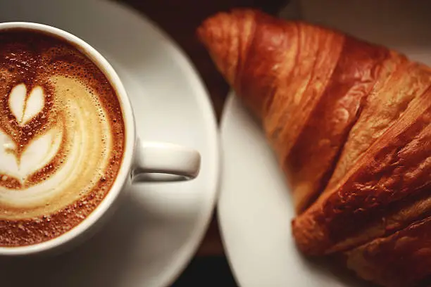 White cup of cappuccino with beautiful foam on wooden table. Latte art, macro, top view.