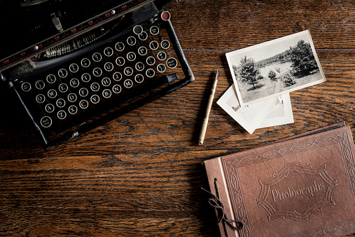 An antique typewriter, pen, photos and a photo album on an old oak table.