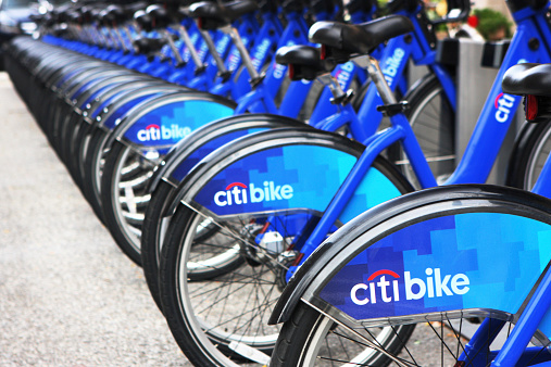 New York City, New York, USA - September 12, 2014: Bicycles are docked at a Citi Bike sharing system kiosk awaiting riders.  The idea for the bike sharing project fomented in 2008 and became a reality in 2013.  Its name is derived from Citigroup, the primary sponsor.  The concept is to provide easy transportation that neither pollutes nor contributes to traffic congestion.  To operate, a rider simply swipes his credit card into the kiosk keypad to buy a 24-hour or 7-day time period access pass.  A $101 security deposit is recorded by the kiosk software.  A bike is selected and undocked.  The seat is adjusted, then the rider proceeds.  Upon return, when the bike is re-docked, another swipe of the pass indicates if credit time is remaining or if additional payment is required.  There are over 300 kiosk locations in the city, with thousands of bikes available.
