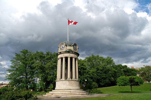 The clock tower in Kitchener's Victoria Park with the Canadian Flag against a dark storm clouds. Nice summer scene with sunlight illuminating clock tower for great contrast.