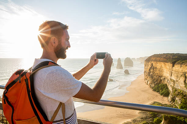 Tourist photographs the Twelve Apostles using mobile phone Cheerful young man takes a picture using a mobile phone of the Twelve Apostles sea rocks on the Great Ocean Road in Victoria's state of Australia. twelve apostles sea rocks victoria australia stock pictures, royalty-free photos & images