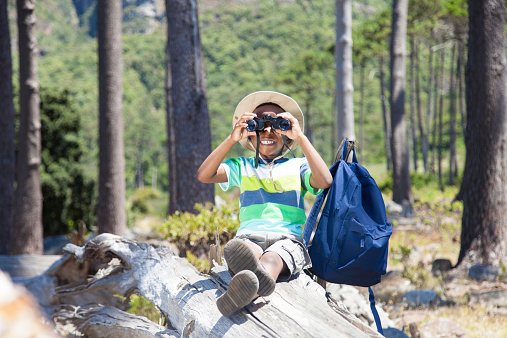 African boy sitting on a log smiling with his binoculars in his hands. Cape Town, Western Cape, South Africa