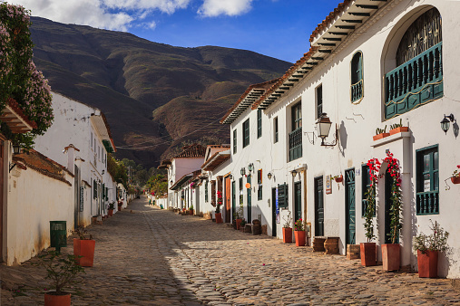 Villa de Leyva, Colombia - September 14, 2014:  It is Sunday morning in Villa de Leyva and Calle or Street 14 is almost lifeless.  The shops and restaurants will open; but, only towards noon.  Founded in 1572 and located at just over 7000 feet above sea level on the Andes Mountains, Villa de Leyva was declared a National Monument in 1954 to protect it's colonial architecture and heritage. It is located in the Department of Boyaca, in the South American country of Colombia.  In the background are the always present Andes Mountains.  Photo shot in the morning sunlight; horizontal format. Copy space.