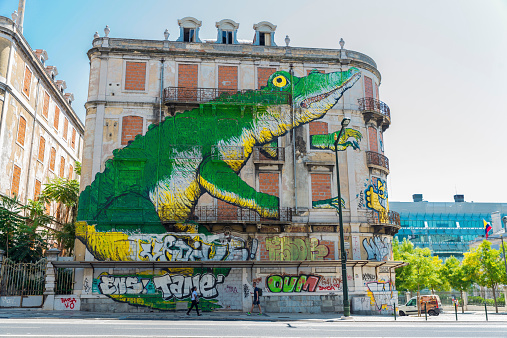 Lisbon, Portugal - August 17, 2014: Graffiti of a giant crocodile on the facade of an abandoned building. A boy and a girl walking down the street