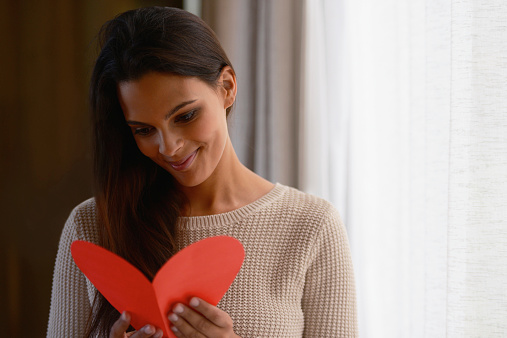 Shot of an attractive young woman reading a valentine's day card at home