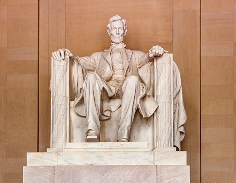 A low angle view of the statue of US President Abraham Lincoln, located in the Lincoln Memorial in Washington DC, against a black background.