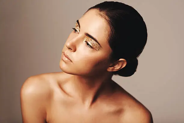 Studio shot of a beautiful woman looking away while wearing nothing but gold make up