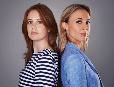 Cropped portrait of two attractive women standing back-to-back in the studio