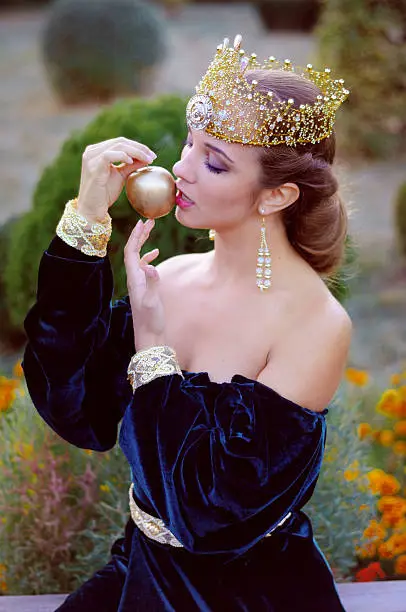 Beautiful young queen wearing a golden crown holding an apple and going to bite