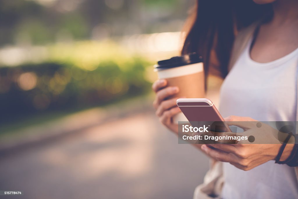 Text messaging Close-up image of woman texting and drinking coffee outdoors Mobile App Stock Photo