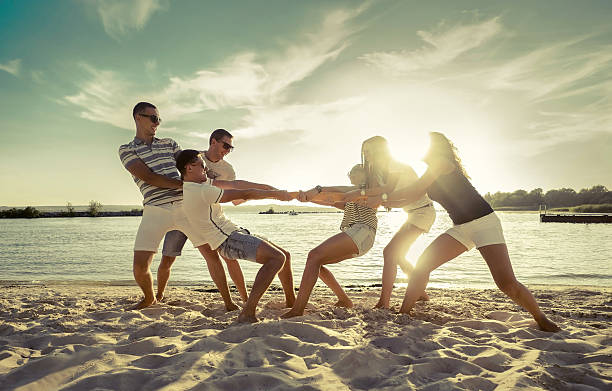 Friends Funny Tug Of War On The Beach Under Sunset Stock Photo - Download  Image Now - Tug-of-war, Beach, Adult - iStock