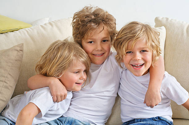 trzy brothers objąć na kanapie - child laughing blond hair three people zdjęcia i obrazy z banku zdjęć