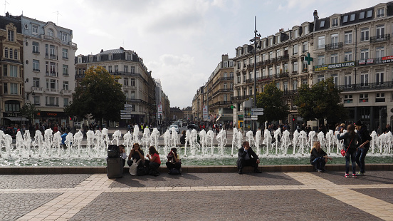 Lille, Paris - August 27, 2014: Traveling People sitting before a fountain on a square in the center of Lille. The fountain is before the railway station.