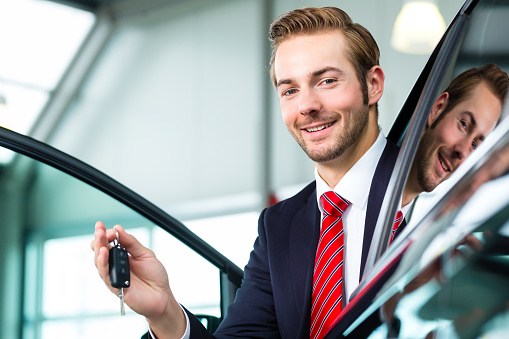 Seller or car salesman in car dealership with key presenting his new and used cars in the showroom