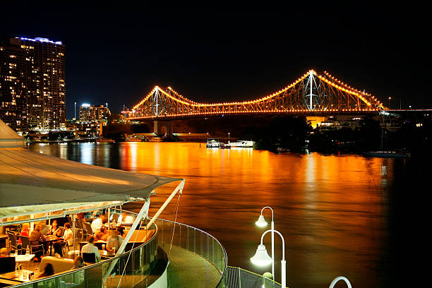 Brisbane, Australia - May 3, 2007: Several groups of people enjoy alfresco dining on the waterfront in Brisbane.  In the background, the lights of the famous Story Bridge reflect in the still waters of the Brisbane River.