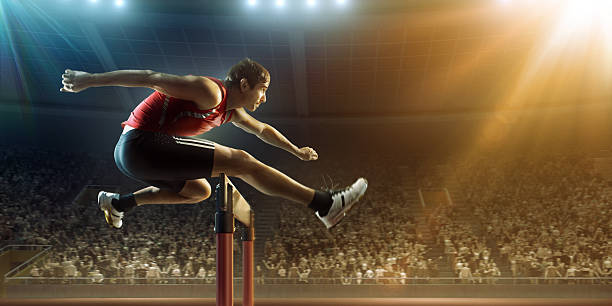 Male athlete hurdling on sports race :biggrin:A professional male athlete jumping over a hurdle during a race. The action takes place in a outdoor . stadium full of spectators. The athlete is wearing generic athletics kit. Low angle image. hurdling track event stock pictures, royalty-free photos & images