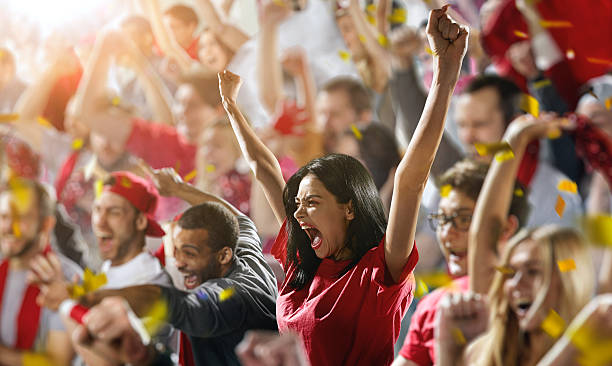 Sport fans: A girl shouting :biggrin:On the foreground a group of cheering fans watch a sport championship on stadium. In the centre a girl shouting putting hands in the air. Everybody are happy. People are dressed in casual cloth. Colourful confetti flies int the air. sports event stock pictures, royalty-free photos & images