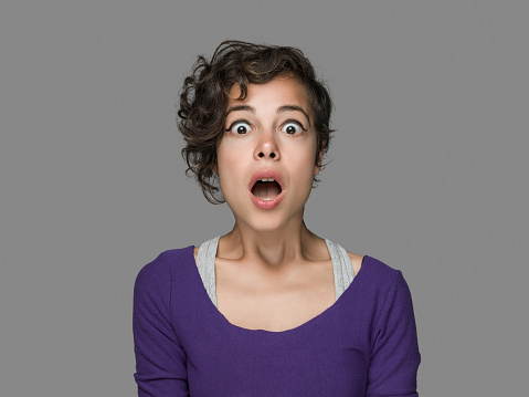 Young woman making a scared face expression over isolated gray background, studio shot. Image taken with Hasselblad H3D camera system and developed from camera RAW.