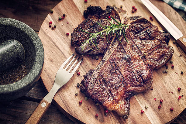 Medium Roasted T-Bone Steak Delicious T-Bone Steak Medium Roasted with Herbs and Pepper. The steak is on a wooden plate served with knife and fork. porterhouse steak stock pictures, royalty-free photos & images