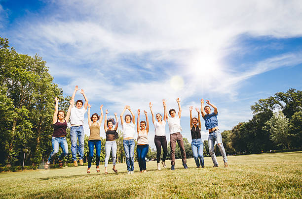 gruppo di amici saltando nel parco - arms raised green jumping hand raised foto e immagini stock