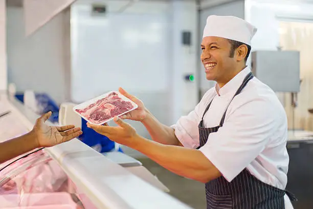 Photo of middle aged butcher serving customer