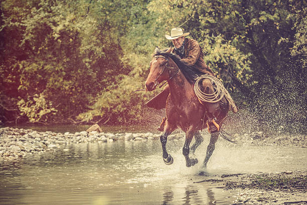 istock Cowboy riding across a river in the forest 515827630