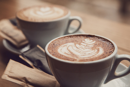 Two perfect cups of cappuccino on a wooden table, close-up.